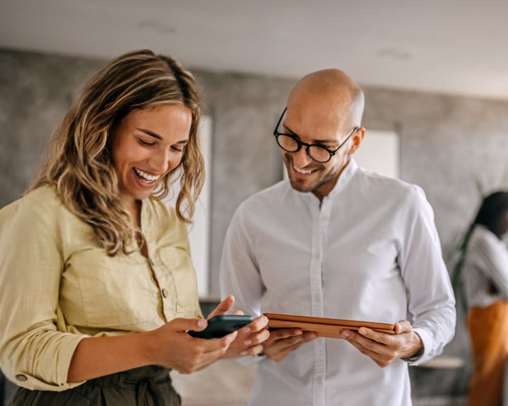 two people smiling and holding digital devices